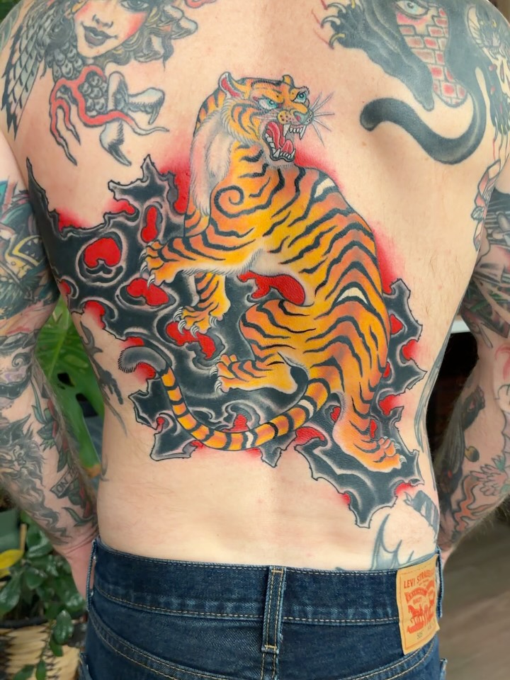 An orange tiger, black rocks and red background tattooed on a back by Chris Astrologo