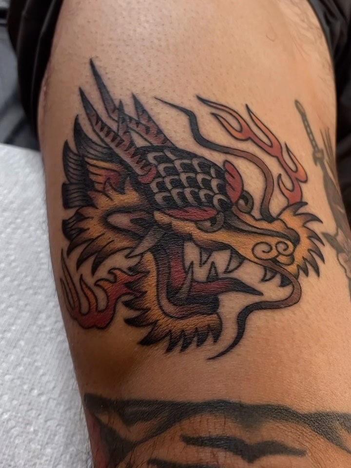 A golden, red and black dragon head tattoo by Jeffrey Bowser