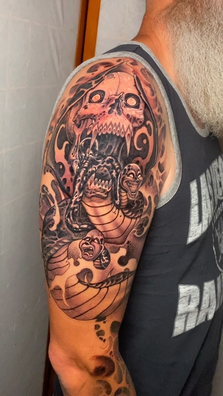 A black-and-gray reaper and snake upper-arm tattoo by Jessi Drahks